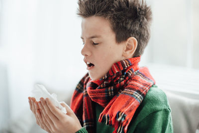 Close-up of boy sneezing at home