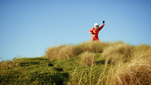 Low angle view of young woman jumping on field against clear sky