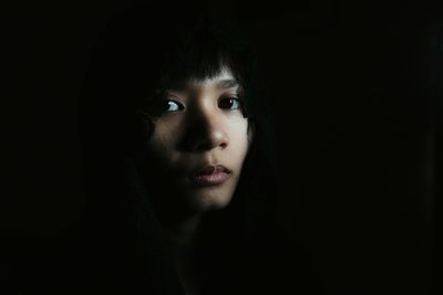 Close-up portrait of young woman against black background