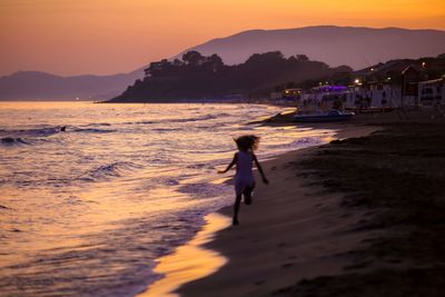 Woman walking on beach against sky during sunset
