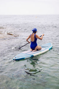 Athlete woman in blue swimsuit and bandana on stand up paddle board. sup surfing