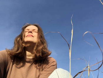 Low angle portrait of woman standing against blue sky