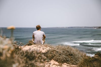 Rear view of man looking at sea against clear sky