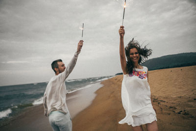 Happy friends enjoying at beach against sky