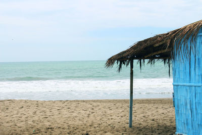 Thatched roof hut on sand at beach against sky