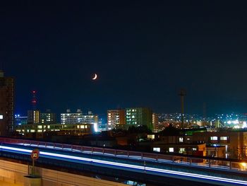 Light trails on road amidst buildings against sky at night