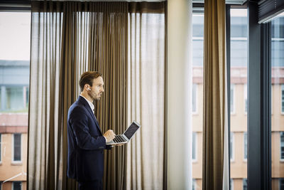 Side view of mid adult lawyer wearing blue tooth while using laptop at office