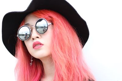 Portrait of beautiful woman wearing sunglasses and hat standing against white background