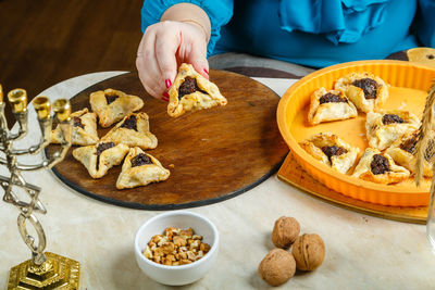 A jewish woman stacks gomentashi cookies for the purim holiday on a wooden board.