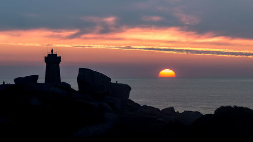 Silhouette rocks by sea against sky during sunset