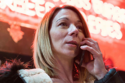 Close-up of woman talking on smart phone against illuminated shop