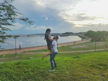 Full length of mother and daughter on grassy field by sea against sky