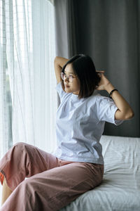 Young woman looking away while sitting on bed at home