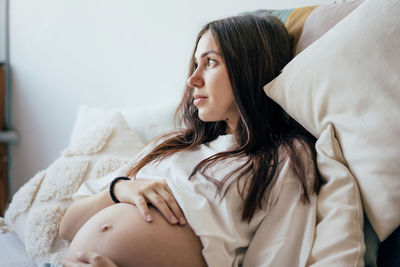 Portrait of attractive pregnant young brunette woman lying on the bed and gently touching her belly.