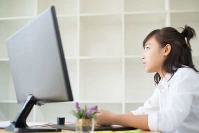 Side view of thoughtful teenage girl sitting by desktop computer on table