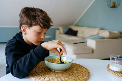 The boy sits over the plate and does not want to have a breakfast. no appetite.