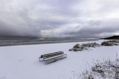 Empty bench on snow covered land against sky