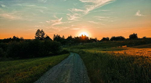 Road amidst field against sky during sunset
