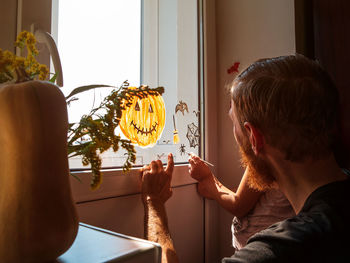 Child and father painting pumpkin on window preparing halloween little girl with dad decorating room