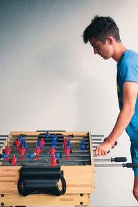 Side view of teenage boy playing foosball against wall at home