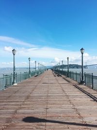 Pier leading towards sea against blue sky