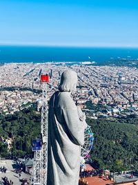 Rear view of statue and woman by sea against sky in city