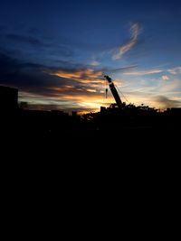 Silhouette cranes against sky at sunset