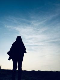 Rear view of silhouette woman standing on field against sky