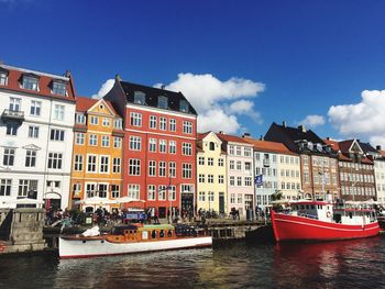 Boats moored on river by buildings against sky