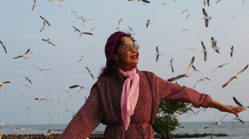 Woman standing with seagulls flying in background at beach