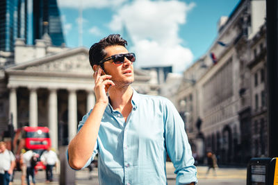 Young man wearing sunglasses standing against city