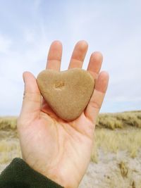 Close-up of hand holding heart shape against sky