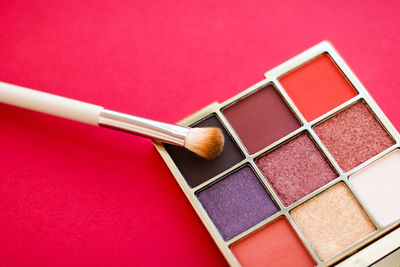 Close-up of multi colored beauty product and make-up brush against pink background