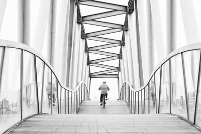 Rear view of person cycling on bridge