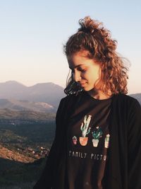 Smiling young woman standing with mountains in background against clear sky