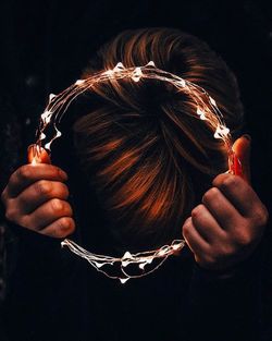 Close-up portrait of woman holding hands against black background