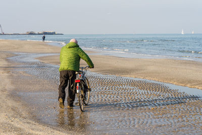 Rear view of man riding bicycle on beach