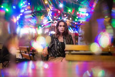 Portrait of young woman sitting in illuminated restaurant at night