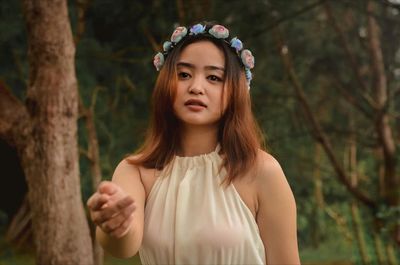 Portrait of beautiful young woman gesturing against trees in forest