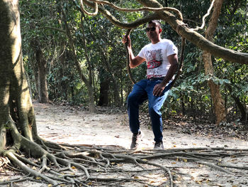 Full length of young man holding tree trunk in forest