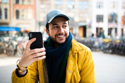 Smiling young man using mobile phone in city