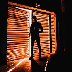 Rear view of man standing against illuminated wall