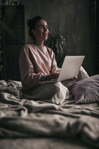 Woman using mobile phone while sitting on bed