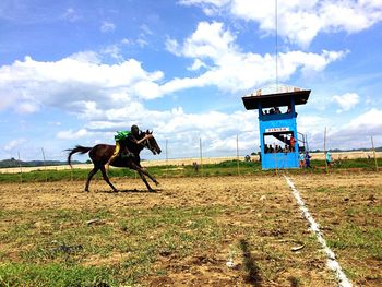 Horse racing on field against sky