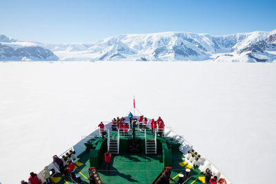 People on cruise ship by snowcapped mountain against sky