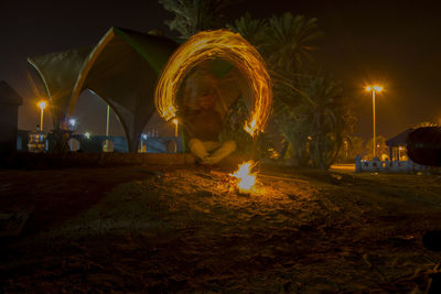 Man sitting at campfire with light painting during night