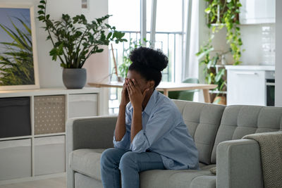 Depressed oppressed african american woman sits on couch flying psychological problems and stress