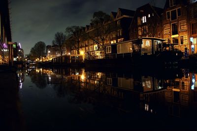 Buildings by calm canal against sky in city at night