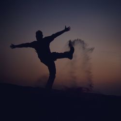 Silhouette of person kicking sand