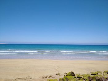 Scenic view of beach against clear blue sky